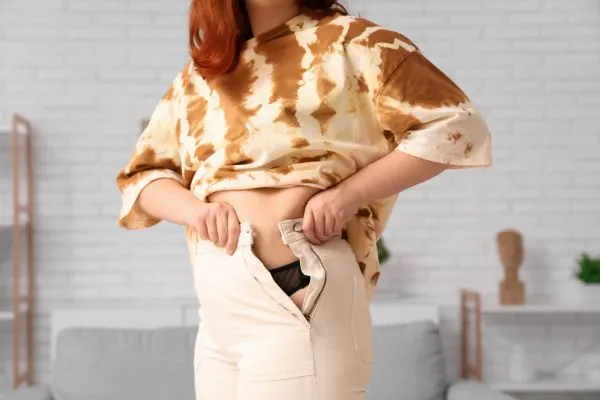 Image of woman trying to do her trousers up after pregnancy weight gain Selston