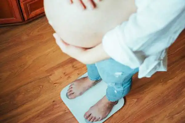 Image of woman weighing herself and experiencing weight gain through pregnancy Selston